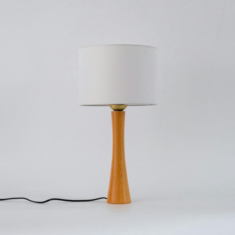 May include: A wooden table lamp with a white fabric shade. The lamp has a slender, tapered base.