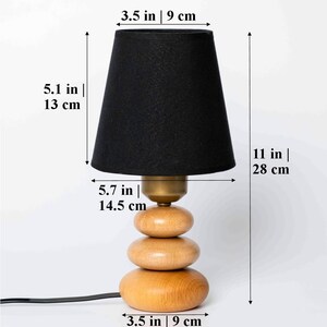 Pode incluir: Um abajur preto com uma base de madeira feita de tr&ecirc;s c&iacute;rculos empilhados. A l&acirc;mpada tem 28 cm de altura e a base 9 cm de largura.