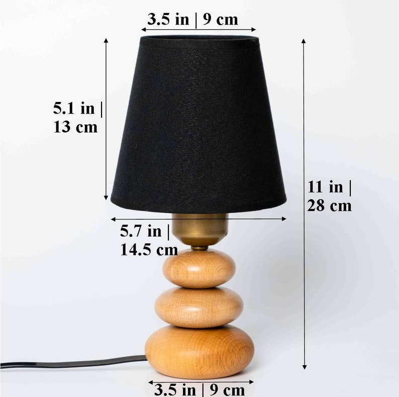 Pode incluir: Um abajur preto com uma base de madeira feita de tr&ecirc;s c&iacute;rculos empilhados. A l&acirc;mpada tem 28 cm de altura e a base 9 cm de largura.