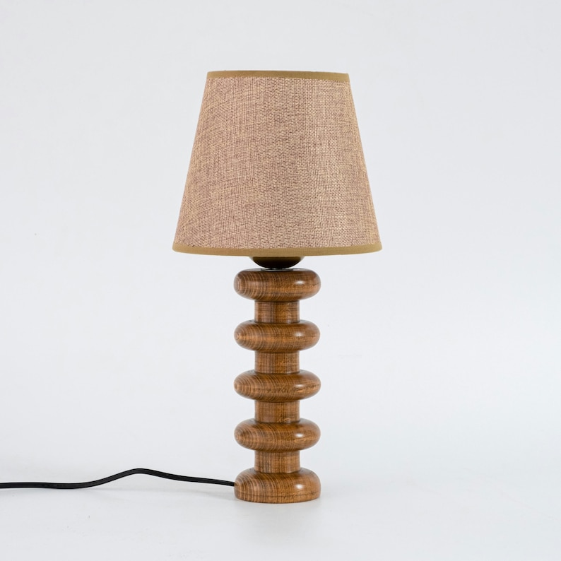 May include: A wooden table lamp with a brown fabric shade. The lamp base is made of stacked wooden circles.