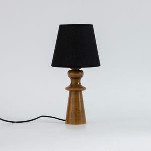 May include: A wooden table lamp with a black fabric lampshade. The lamp has a simple, modern design and is perfect for adding a touch of style to any room.