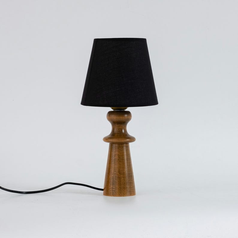 May include: A wooden table lamp with a black fabric lampshade. The lamp has a simple, modern design and is perfect for adding a touch of style to any room.