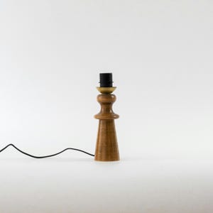May include: A wooden table lamp with a brown wooden base and a black wire. The lamp has a brass socket and a black cord.