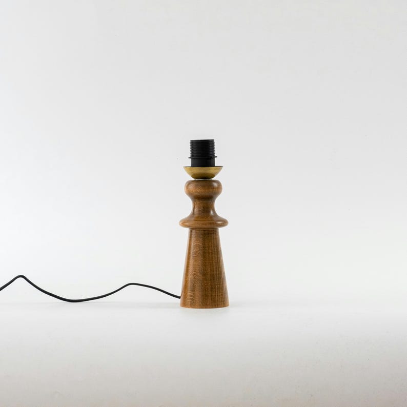 May include: A wooden table lamp with a brown wooden base and a black wire. The lamp has a brass socket and a black cord.