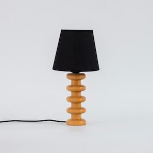 May include: A wooden table lamp with a black fabric shade. The lamp base is made of stacked wooden circles.