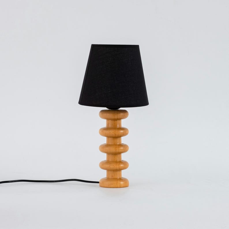 May include: A wooden table lamp with a black fabric shade. The lamp base is made of stacked wooden circles.