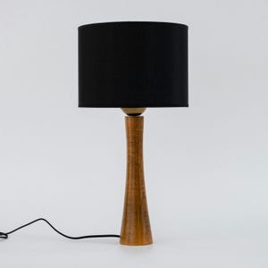 May include: A wooden table lamp with a black fabric lampshade. The lamp has a tall, slender base with a natural wood finish.
