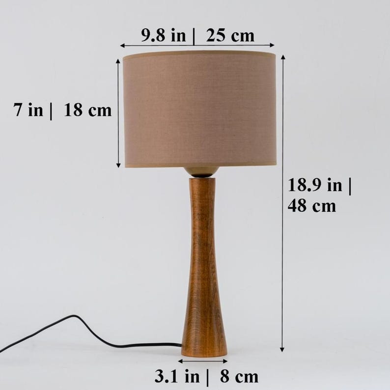 May include: A wooden table lamp with a brown fabric lampshade. The lamp is 18.9 inches tall and the lampshade is 9.8 inches wide. The base of the lamp is 3.1 inches wide.