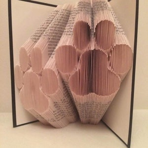 May include: A book art sculpture of two paw prints made from folded pages of a book. The sculpture is displayed open on a black surface.