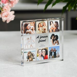 May include: A square clear acrylic photo block featuring a collage of eight photographs of two people. The center of the block displays the black text A forever friend and the names Olivia and Emma. The block has a thick, transparent design.