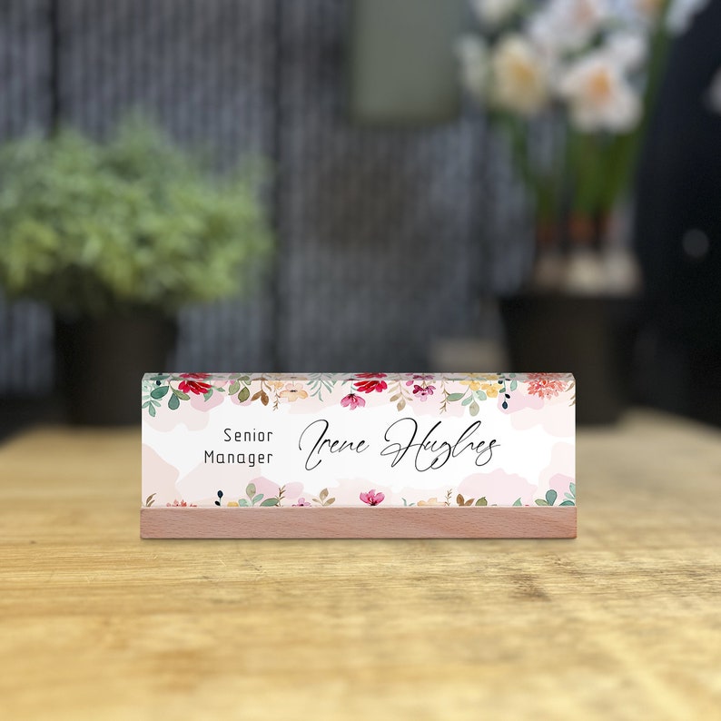 May include: A pink and white desk nameplate with a floral design. The nameplate has a wooden base and reads "Senior Manager Irene Hughes". desk plate, personalized sign, name sign, name plate, name plate for desk, acrylic name plate, custom name plate, job title plate, promotion gift, principal gift, supervisor gifts, coworker gift, elegant desk sign