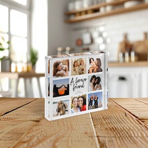 May include: A clear acrylic photo block featuring nine images. The block has the text "A forever friend" with the names Olivia and Emma. The photos depict various people and scenes, including a sunset silhouette and a group of friends.