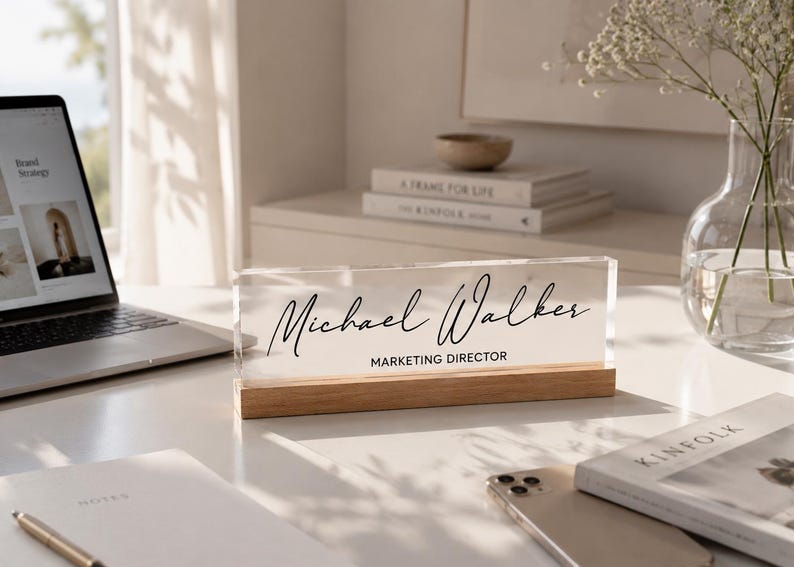 May include: A clear acrylic desk nameplate with the name "Michael Walker" in elegant black script. Below the name, the title "MARKETING DIRECTOR" is printed. The nameplate sits on a wooden base.
