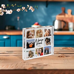 May include: A clear acrylic photo block featuring nine images of friends. The block has the text "A forever friend" with the names Olivia and Emma. The photos are of people, and the block is on a wooden surface.