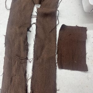 May include: Two long strips of brown fabric with frayed edges and a smaller square piece of the same fabric.