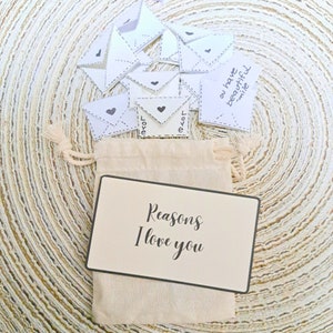 May include: A small white canvas bag with a card that says "Reasons I love you" and a pile of small white envelopes with black hearts and the word "love" written on them.