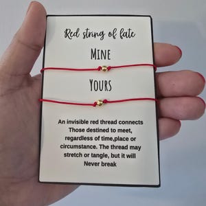 May include: Two red string bracelets with small gold-colored beads mounted on a rectangular white card. The card features the text Red string of fate, MINE, YOURS, and a quote about an invisible red thread that connects those destined to meet.