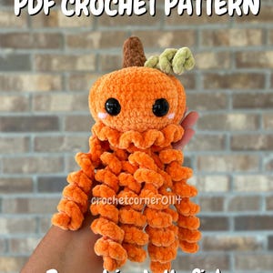 May include: A PDF crochet pattern for a plush pumpkin jellyfish. The toy features a round orange pumpkin head with a brown stem, a light green leaf, and black eyes with pink cheeks. It has many long, curly orange tentacles hanging down.