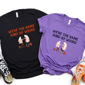 May include: Two black and purple t-shirts with a graphic of two ghosts holding hands and the text "We're the same kind of weird".