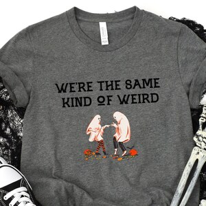May include: Gray t-shirt with a black graphic of two ghosts dancing and the text "We're the same kind of weird".