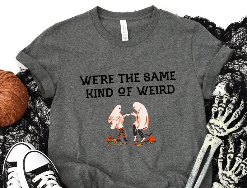 May include: Gray t-shirt with a black graphic of two ghosts dancing and the text "We're the same kind of weird".