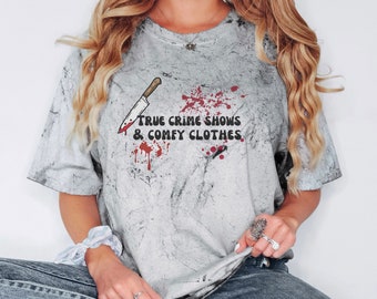 Op de afbeelding: Een grijs T-shirt met een wit en grijs tie-dye patroon. Het shirt heeft een afbeelding van een bloedig mes en de tekst "True Crime Shows & Comfy Clothes".