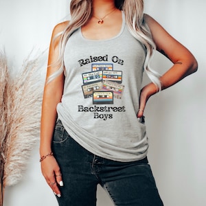 Op de afbeelding: Een grijs tanktop met de tekst "Raised On Backstreet Boys" en een afbeelding van cassettebandjes met songtitels zoals "The Call", "Everybody" en "I Want It That Way".