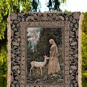 Puede incluir: Una manta de tejido de tapiz presenta a una mujer con un vestido blanco de pie en un bosque con un ciervo blanco. El tapiz está enmarcado con un borde adornado negro y dorado. El texto "INK & SHADOW Original Fine Art Throws" está en la parte inferior de la imagen.