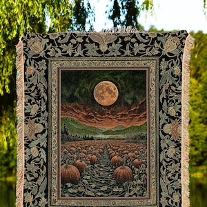 May include: A tapestry throw blanket featuring a full moon over a pumpkin field. The blanket has a black border with floral and leaf patterns and fringe. The text "INK & SHADOW Original Fine Art Throws" is at the bottom.