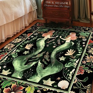 May include: A dark green area rug features two mermaids with flowing tails, surrounded by floral and shell designs. The rug has a black background with gold accents. The text 'INK & SHADOW Original Fine Art Rugs' is visible on a wooden nightstand in the background. The rug is displayed in a bedroom setting with a wooden bed and light teal curtains.