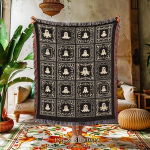 May include: A black and cream-colored throw blanket featuring a repeating pattern of ghost figures within decorative squares. The blanket has a fringed edge and is displayed indoors. The text "INK & SHADOW Original Fine Art Throws" is visible at the bottom.