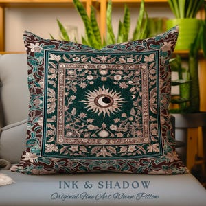Könnte beinhalten: Ein quadratisches Zierkissen mit dunkelgrünem Hintergrund, einem zentralen Sonnen- und Mondsichelmotiv sowie komplizierten Blumenmustern in Creme-, Braun- und Petroltönen. Der Text INK & SHADOW Original Fine Art Woven Pillow ist zu sehen.