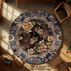 May include: Round area rug with a dark blue border featuring floral and scrollwork patterns. The center design showcases bats, flowers, and foliage. The rug has the text "INK & SHADOW Original Fine Art Rugs" at the bottom.