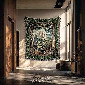 May include: A rectangular woven tapestry blanket featuring a detailed landscape scene of a castle nestled among trees and hills. The design is framed by a wide, dark green border with floral patterns and has fringed edges on all four sides.