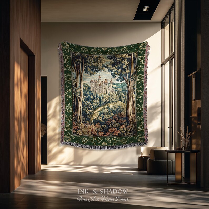 May include: A rectangular woven tapestry blanket featuring a detailed landscape scene of a castle nestled among trees and hills. The design is framed by a wide, dark green border with floral patterns and has fringed edges on all four sides.