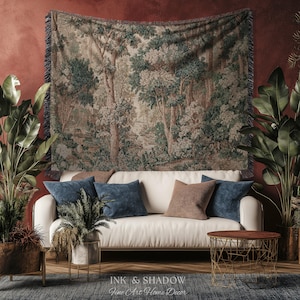 May include: A tapestry depicting a forest scene hangs above a white sofa with blue and brown throw pillows. The room is decorated with potted plants and a small, round table. The text "INK & SHADOW Fine Art Home Decor" is at the bottom.