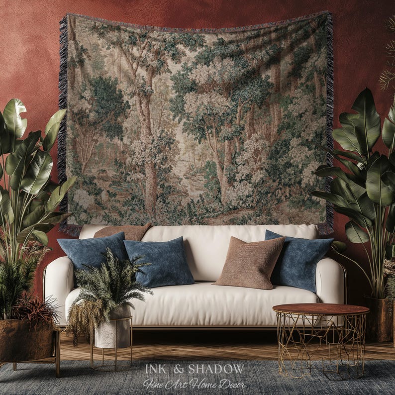 May include: A tapestry depicting a forest scene hangs above a white sofa with blue and brown throw pillows. The room is decorated with potted plants and a small, round table. The text "INK & SHADOW Fine Art Home Decor" is at the bottom.