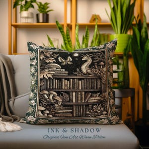 May include: A green and gold woven pillow with a dragon perched on a bookshelf filled with books. The pillow features a dark background with a moon and stars. The text "INK & SHADOW Original Fine Art Woven Pillow" is printed on the bottom of the pillow.