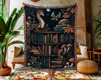 May include: A tapestry throw blanket featuring a fantasy scene with a dragon, mushrooms, and a bookshelf filled with books. The throw has a dark background with a fringed edge and the text "INK & SHADOW Original Fine Art Throws" at the bottom.