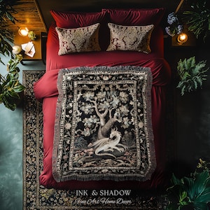 May include: A woven throw blanket featuring a detailed illustration of a white dragon resting beneath a large tree, set against a dark background with floral borders. The blanket is draped over a bed with deep red bedding and two patterned pillows.