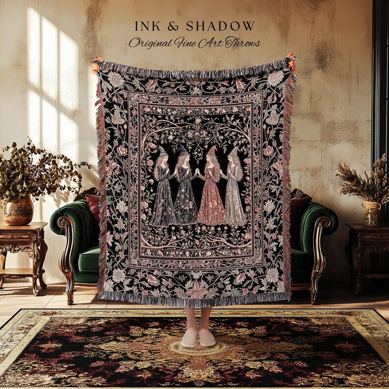 May include: A woven throw blanket featuring a central illustration of four figures in pointed hats standing in a circle, surrounded by a detailed floral border in black, pink, and cream tones. The text INK & SHADOW Original Fine Art Throws is visible.