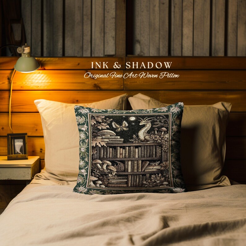 May include: A green pillow with a woven tapestry design featuring a bookshelf filled with books, a dragon, and a butterfly. The pillow has the text "INK & SHADOW Original Fine Art Woven Pillow" on it.