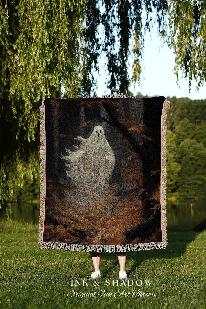 May include: A woven throw blanket featuring a ghostly figure in a dark forest scene. The blanket has a black background with brown and gray accents, and a fringe border. The text "INK & SHADOW Original Fine Art Throws" is at the bottom.