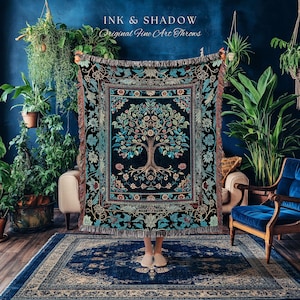 May include: A decorative throw blanket with a tree of life design in teal, blue, and brown on a black background. The blanket has a fringed edge and the text "INK & SHADOW Original Fine Art Throws". The blanket is held up in front of a person.