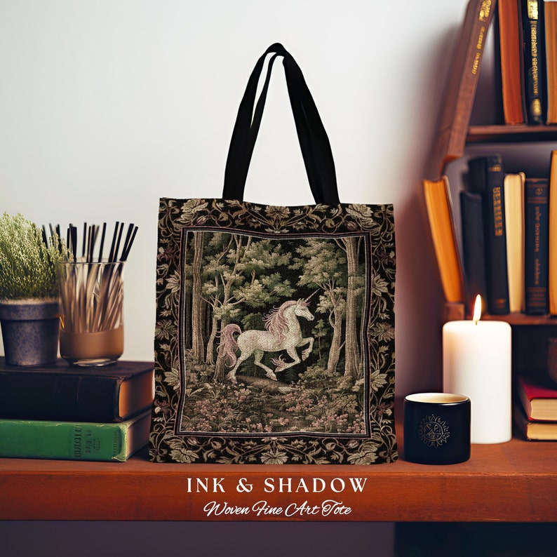 Może przedstawiać: Czarna torba typu tote z tkaniny z motywem gobelinu przedstawiającym białego jednorożca w lesie. Torba ma czarne uchwyty i napis "INK & SHADOW Woven-Fine Art Tote" nadrukowany na dole.