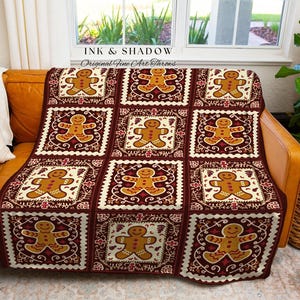 May include: A gingerbread-themed throw blanket with a repeating pattern of gingerbread men on a burgundy background. The blanket is draped over a brown leather couch, with a white pillow and a houseplant in the background. The text "INK & SHADOW Original Fine Art Throws" is visible.