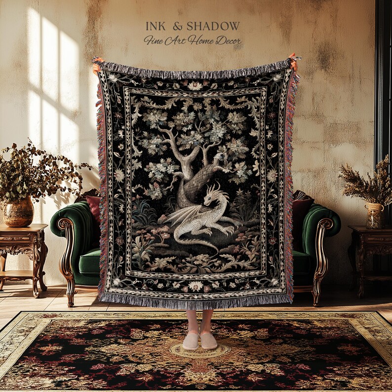 May include: A woven throw blanket featuring a central illustration of a white dragon resting beneath a large tree on a black background. The blanket has a decorative floral border and fringed edges. The text INK & SHADOW Fine Art Home Decor is visible.