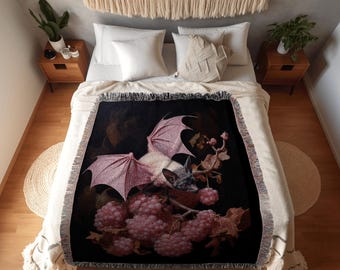 Puede incluir: Una manta negra con un diseño de murciélago con alas rosas, rodeado de bayas y hojas rosas. La manta tiene un borde con flecos y el texto "INK & SHADOW Original Fine Art Throws".