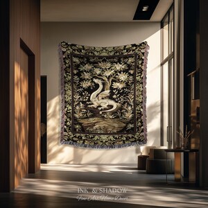 May include: A woven tapestry blanket featuring a central white dragon illustration set against a black background with a detailed tree and floral border. The edges are finished with a fringed trim. The text INK & SHADOW Fine Art Home Decor is visible.