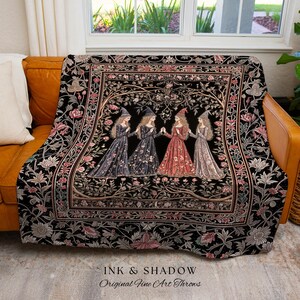 May include: A woven throw blanket featuring a black background with a central rectangular panel depicting four figures in pointed hats and long dresses standing among stylized trees and flowers. The border displays floral patterns in pink and white.